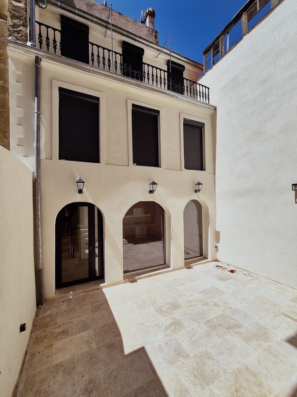 La même cour après rénovation : façade ravalée, arches vitrées et sol en travertin